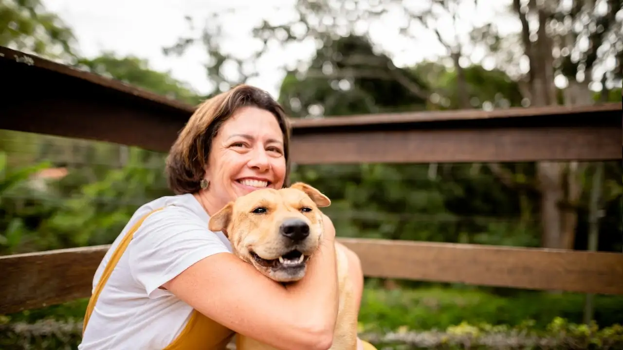 Smiling mature woman giving her cog a big hug while sitting together outside on her patio in her back yard