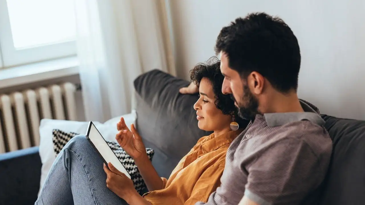 A happy couple sitting on the cozy sofa at home and going over their finances