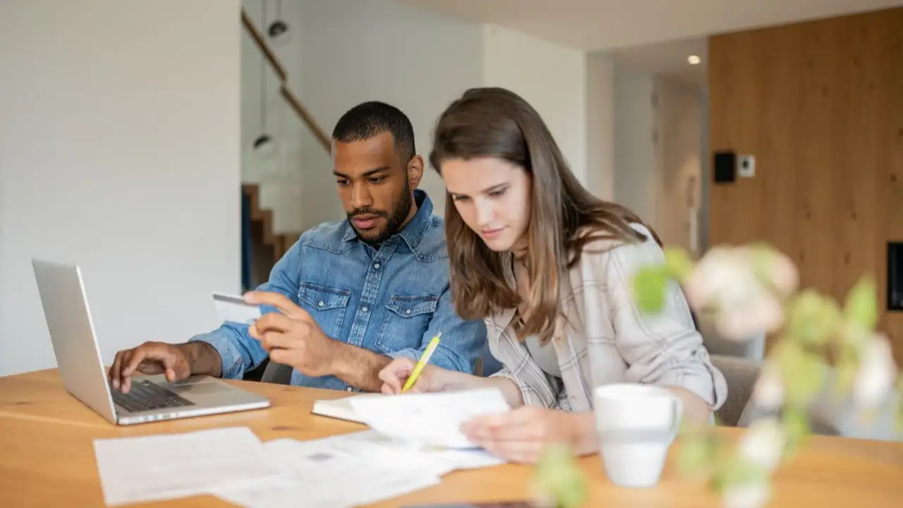 At the table in the living room, a  couple examines credit report and their bank accounts.