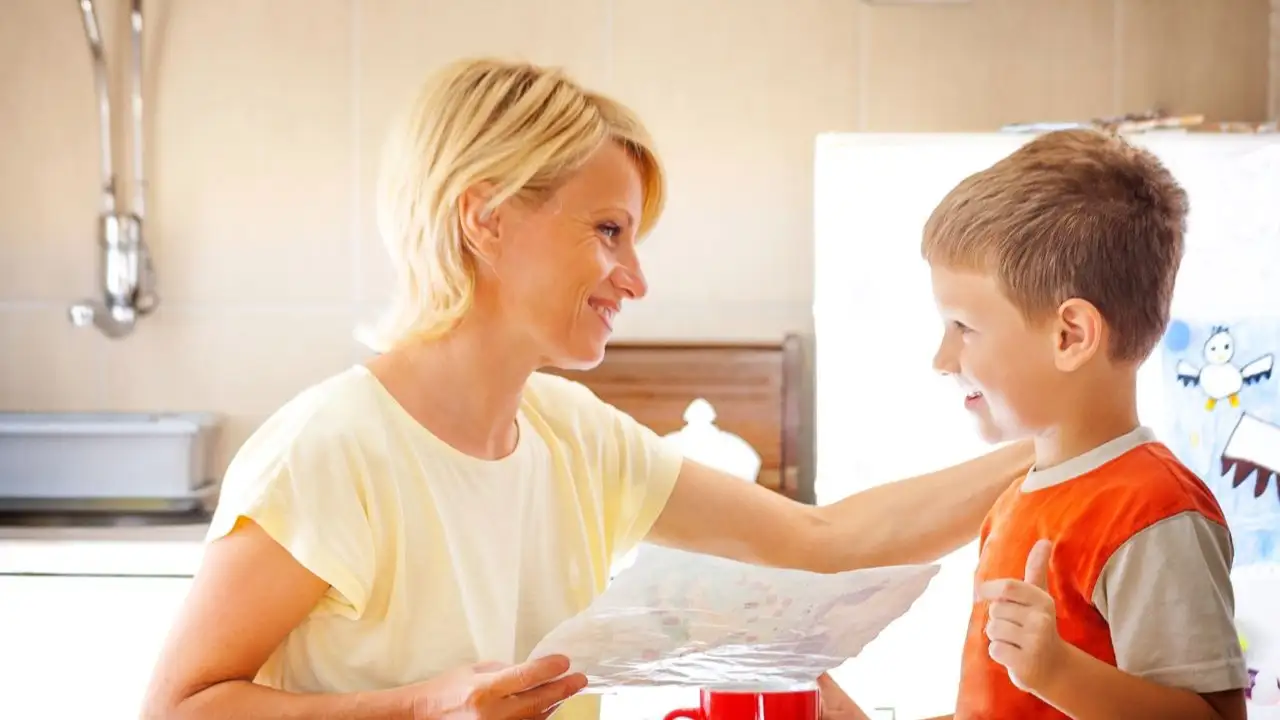 Son showing his drawing to mother while she was looking through bills and sitting at dinning table in the kitchen