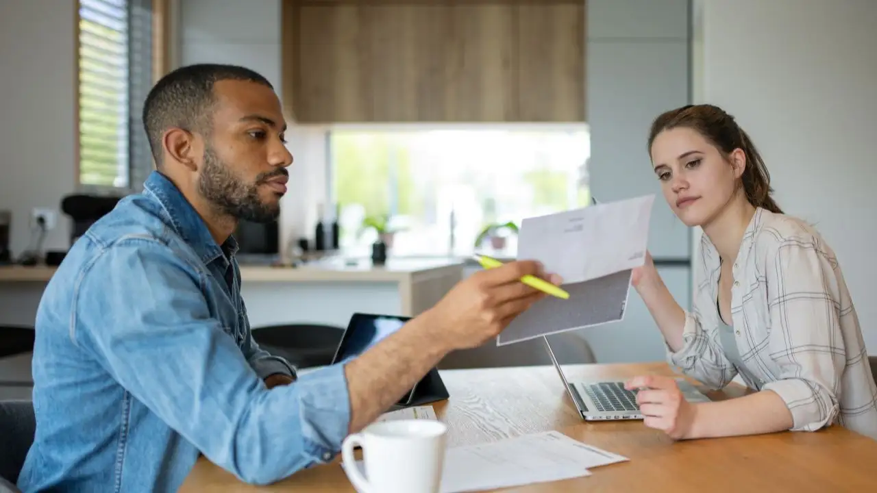 At the table in the living room, a couple examines finance papers