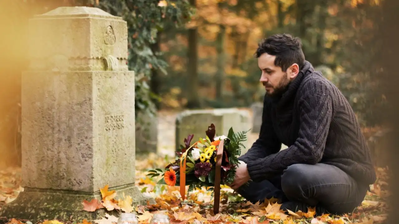 Mid adult man with flowers and candles visiting graves at the cemetery.