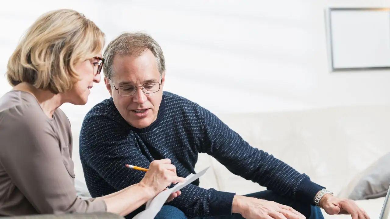 A mature couple at home sitting in their living room looking at bills