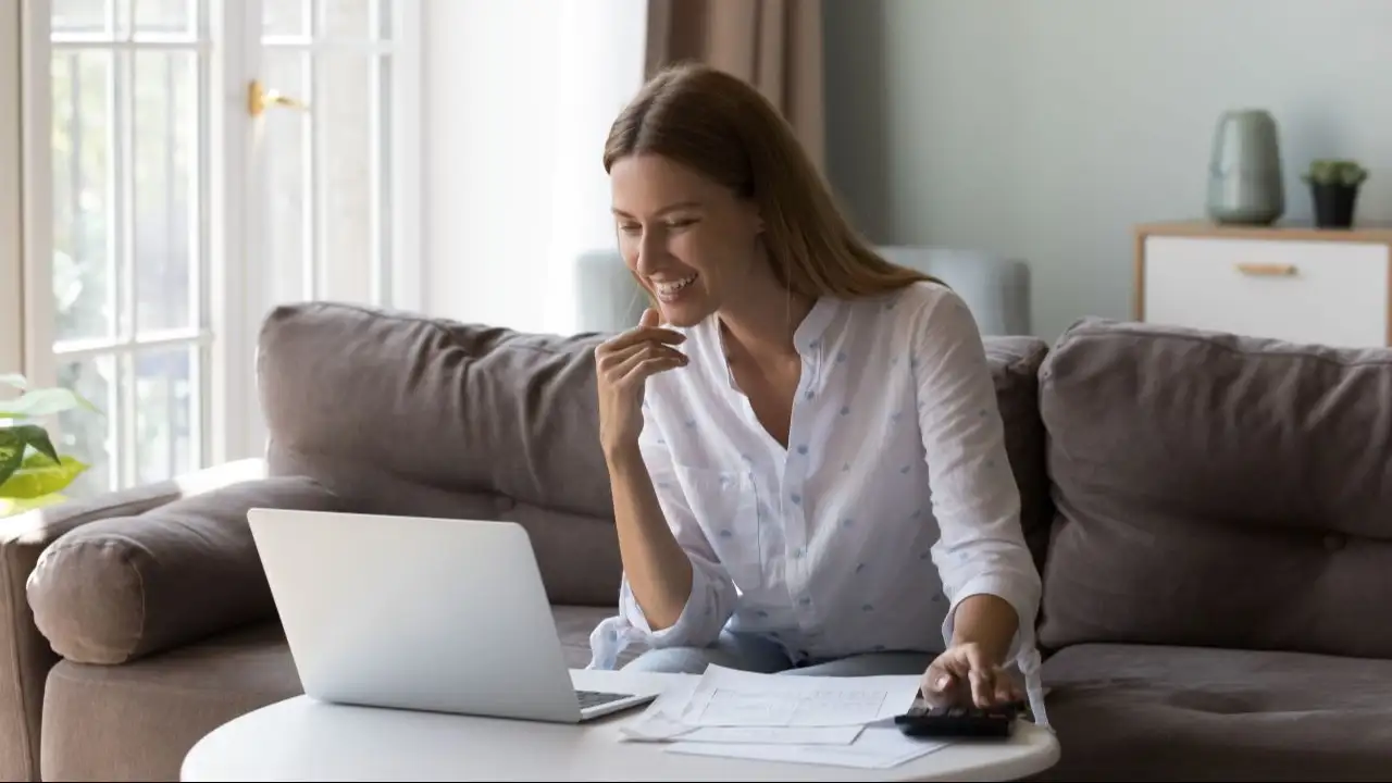 Woman sits at table with laptop counts incomes looks satisfied