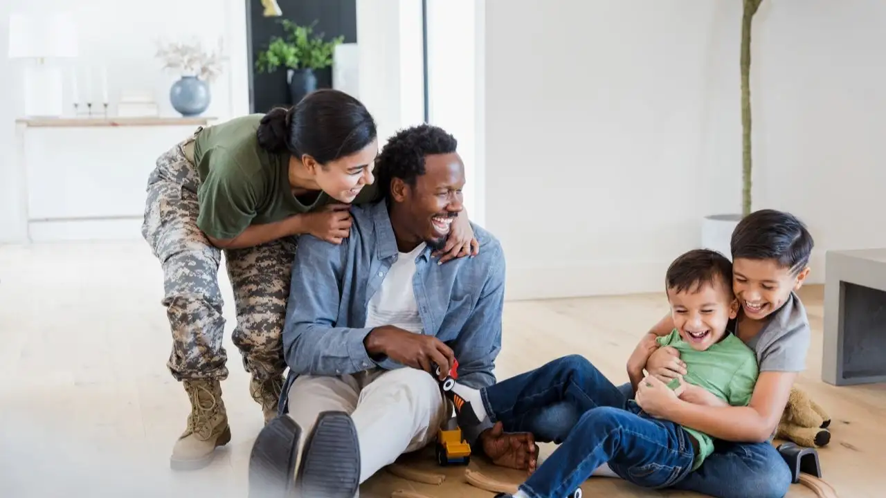 Veteran mother and husband smile as they watch their two boys laughing and wrestling on the living room floor.