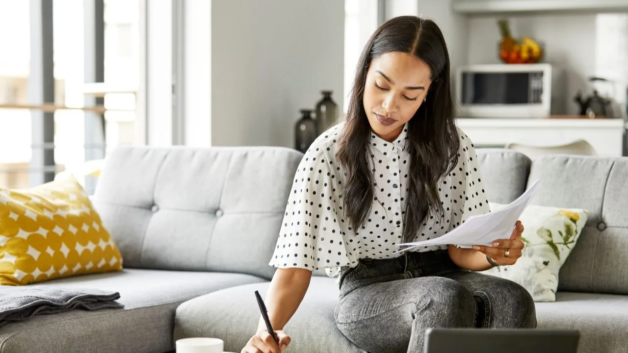 A woman analyzes bills using a digital tablet at the table and sitting on the sofa at home.