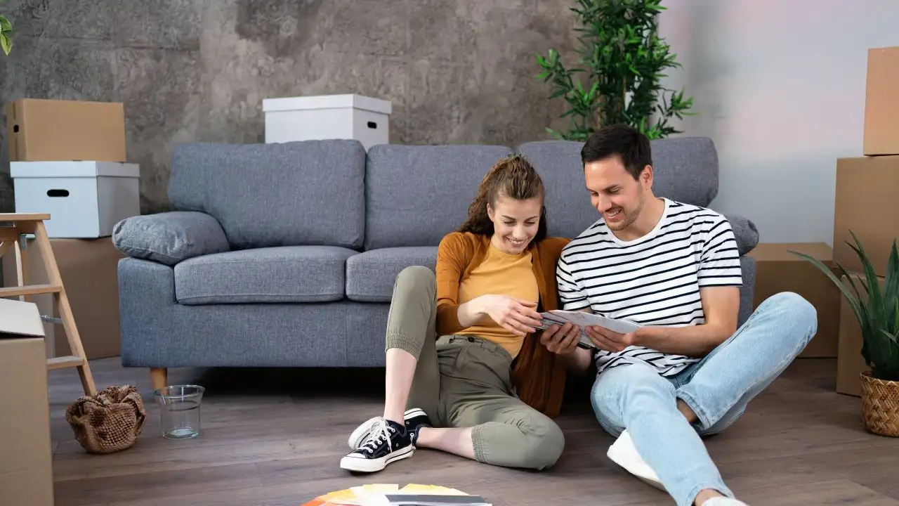 Young couple, sitting on the floor looking at a paint color swatch, while planning a renovation in their new apartment