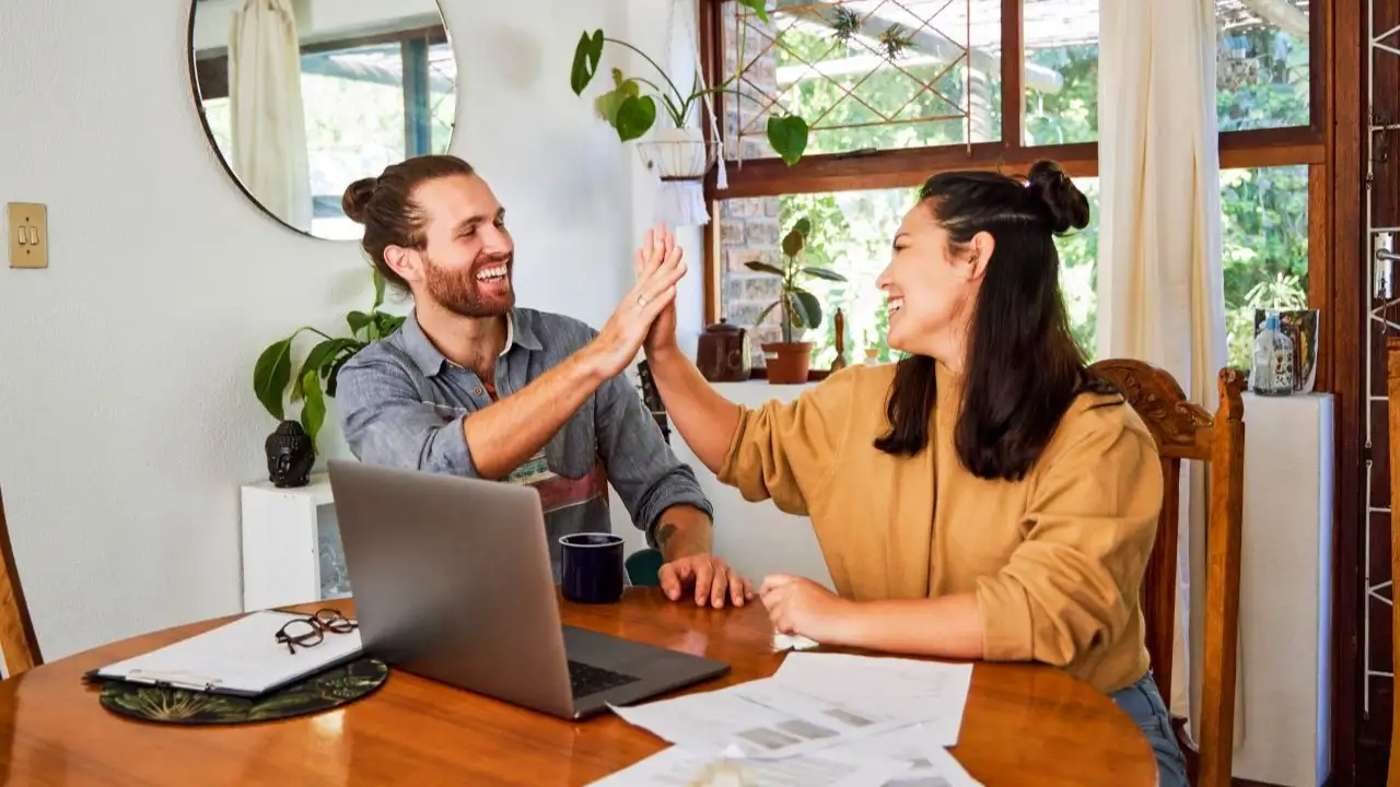 Young couple sharing a high five while using a laptop and checking credit