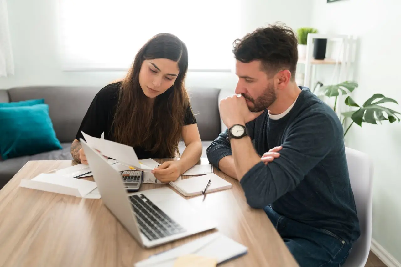 Young couple reviewing finances and debt with a laptop and bills in their living room. 