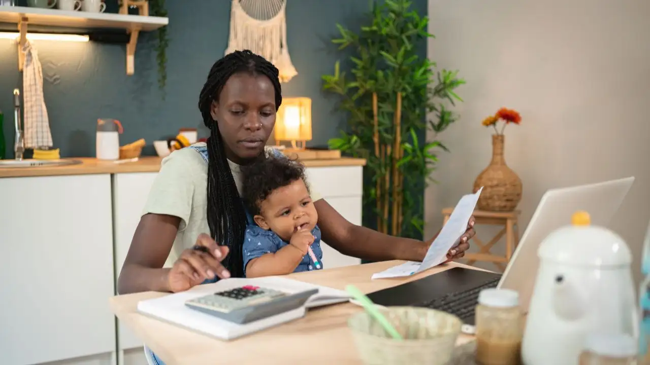 Worried single mother analyzing and calculating her home finances, while her baby boy sitting in her lap