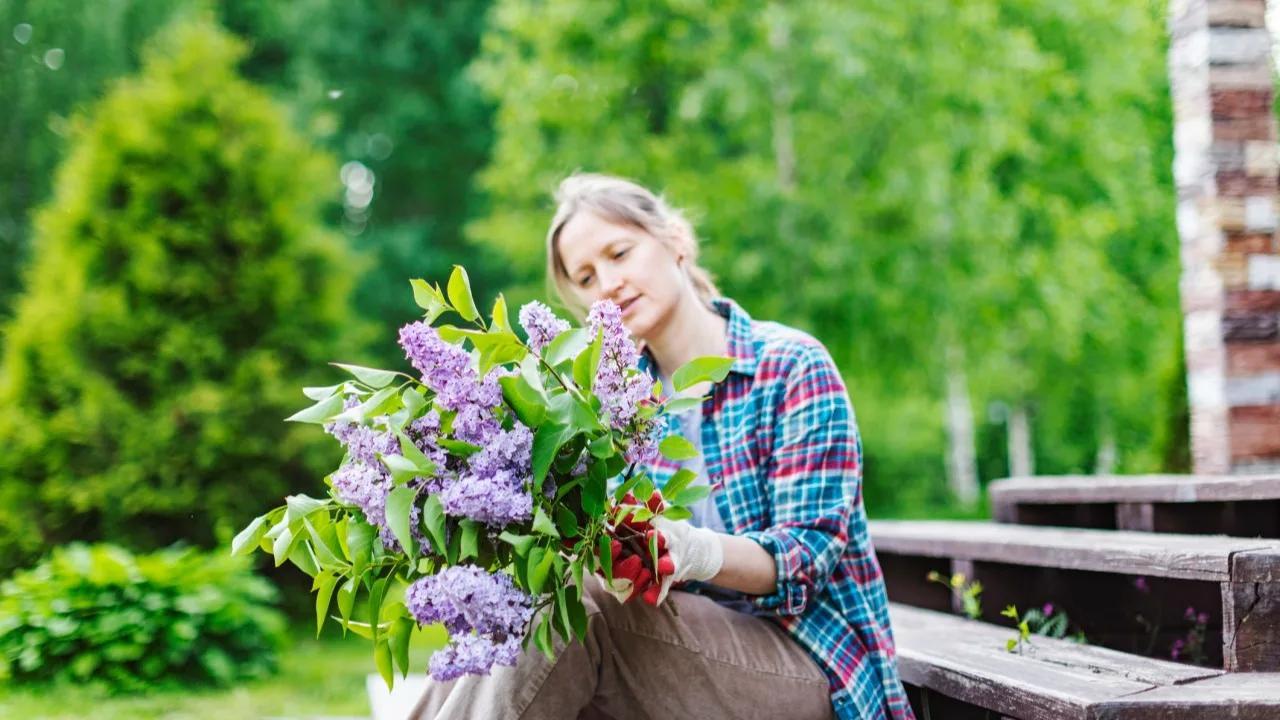 Young adult woman sitting with fresh flowers from her garden on the steps of her house