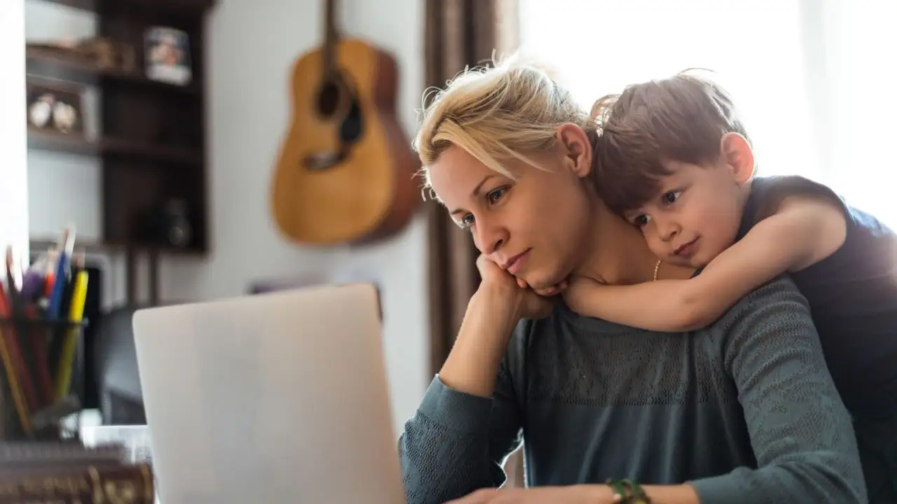 A cute little boy hugging his mom tightly while she is working.