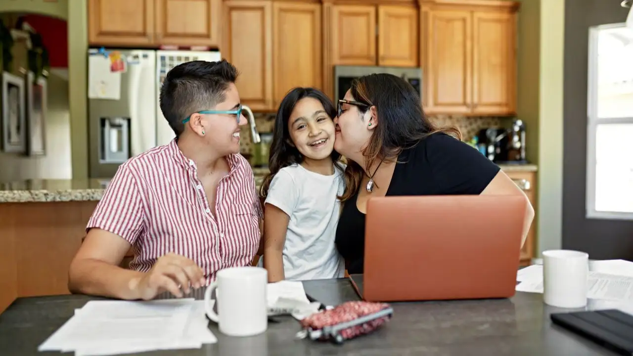 early 30s women pausing from paying bills and discussing the budget to hug and kiss their 8 year old child.