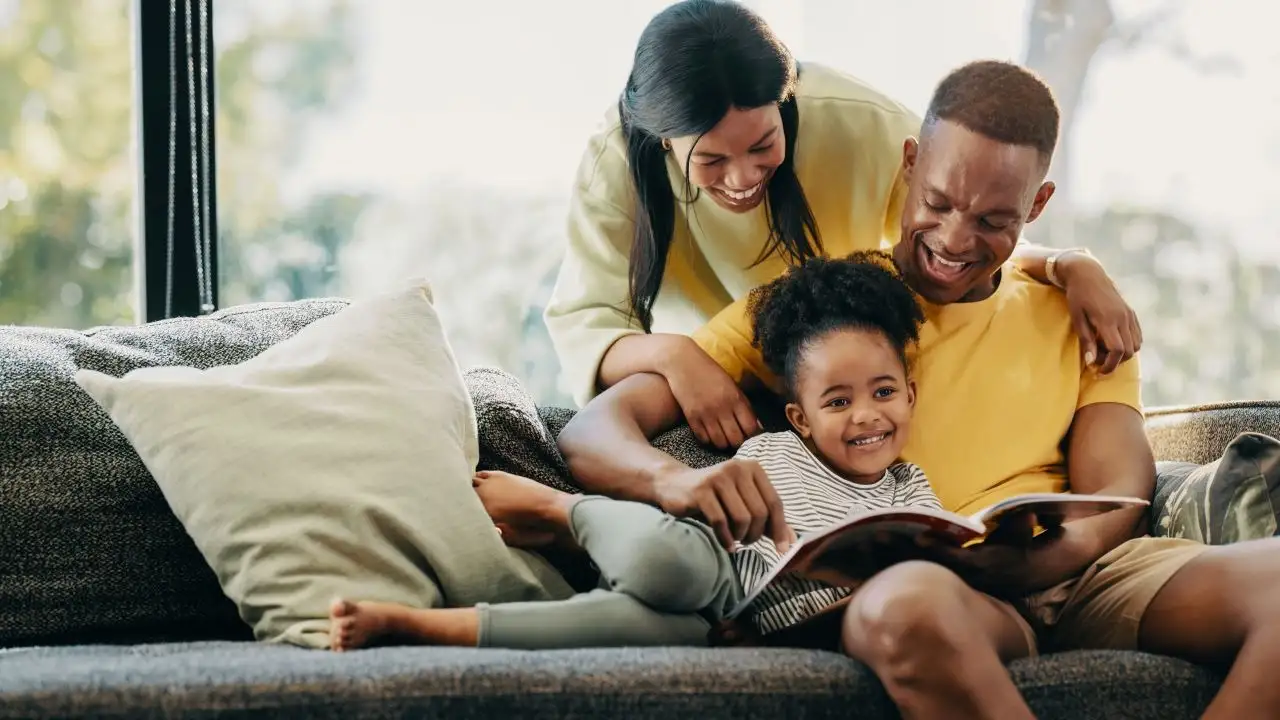 Happy little girl reading a story with her mother and father. Fun family moments on the weekend.