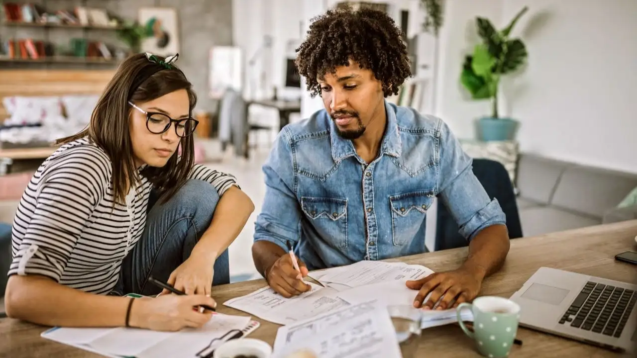 Young couple at kitchen table looking at finances-avoiding debt cycle.