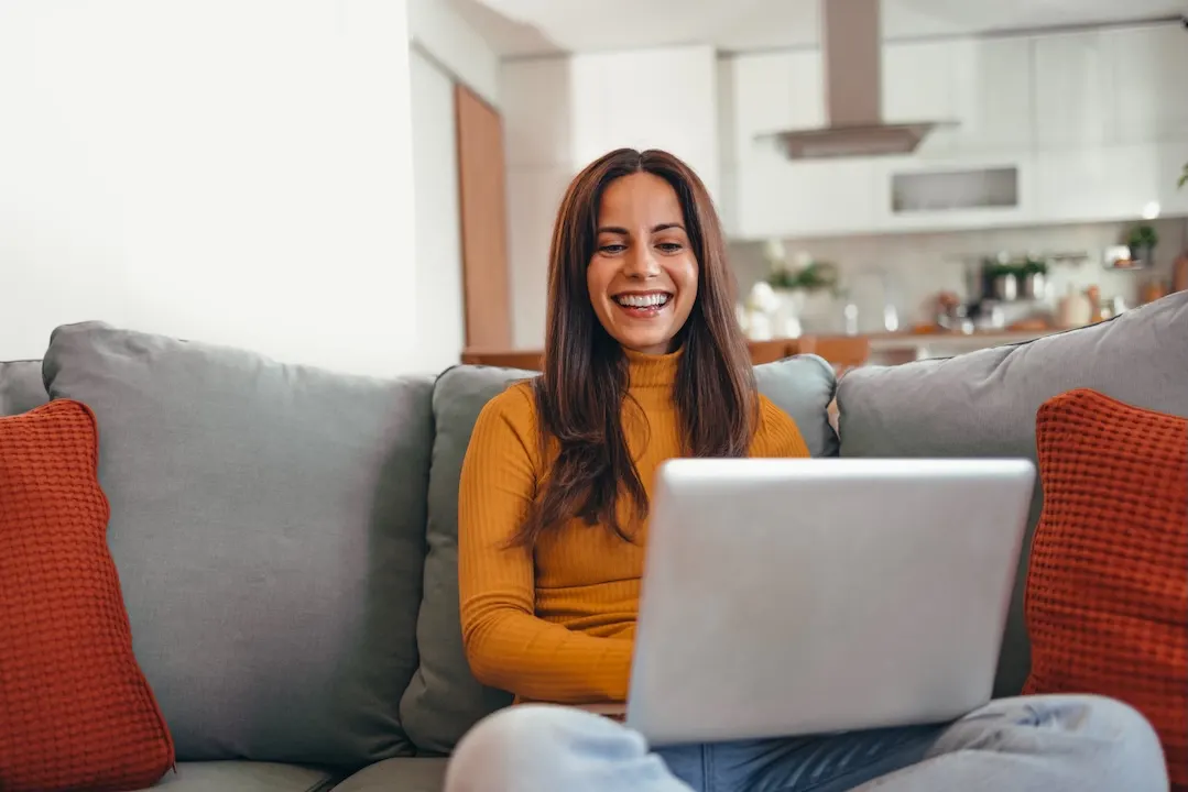 Woman sitting on a couch and using her laptop, looking happy.